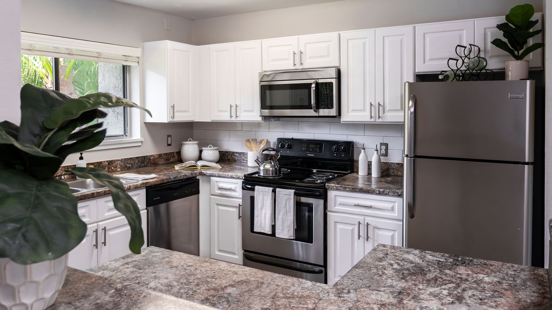 Renovated kitchen with stainless steel appliances, white cabinetry, and granite-style countertops.