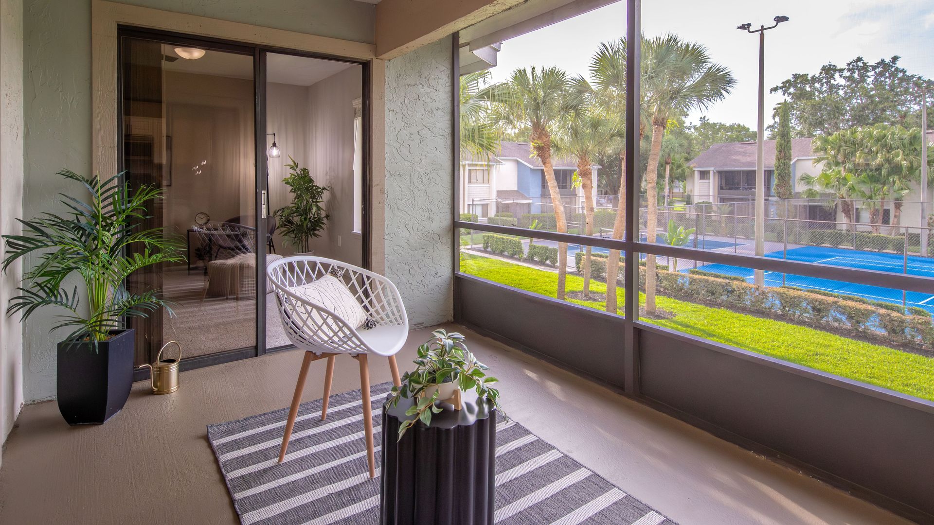 Screened-in patio with modern outdoor furniture and view of tennis courts at Harper Grand Apartments in Orlando, FL.