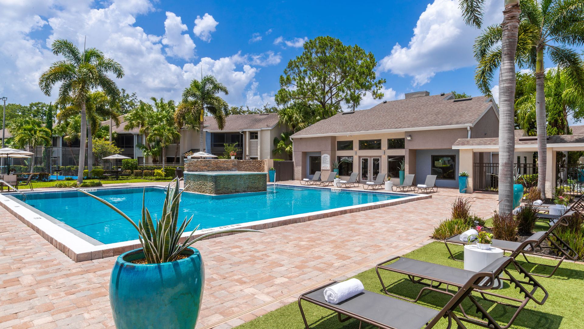 Resort-style swimming pool surrounded by palm trees, lounge chairs, and clubhouse at Harper Grand Apartments in Orlando, FL.