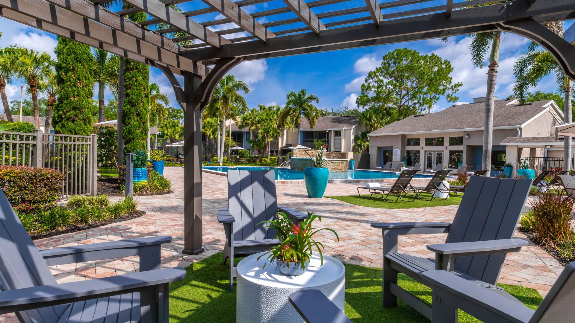 Pergola-covered Adirondack chairs with view of pool, lounge area, and clubhouse at Harper Grand Apartments.