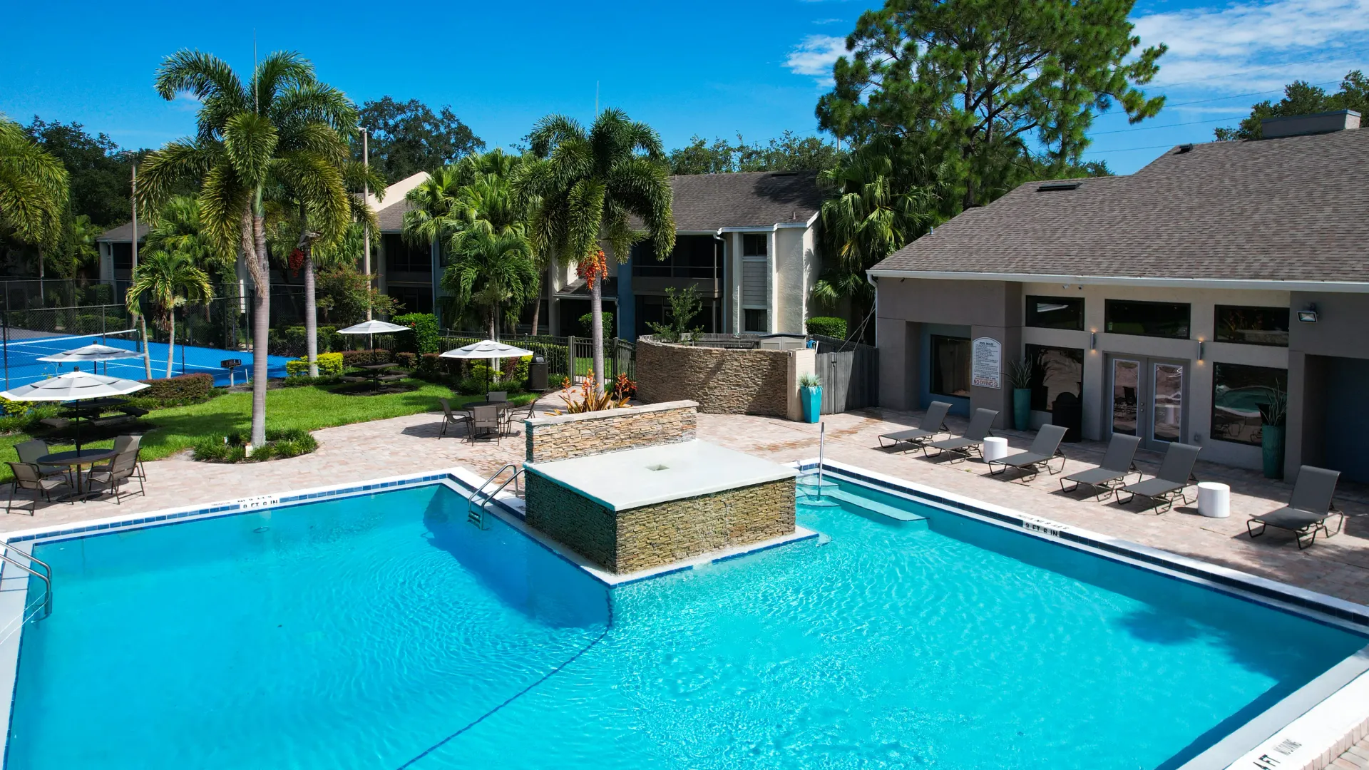 Outdoor pool with palm trees, lounge chairs, and a water feature, providing a tranquil environment for residents.