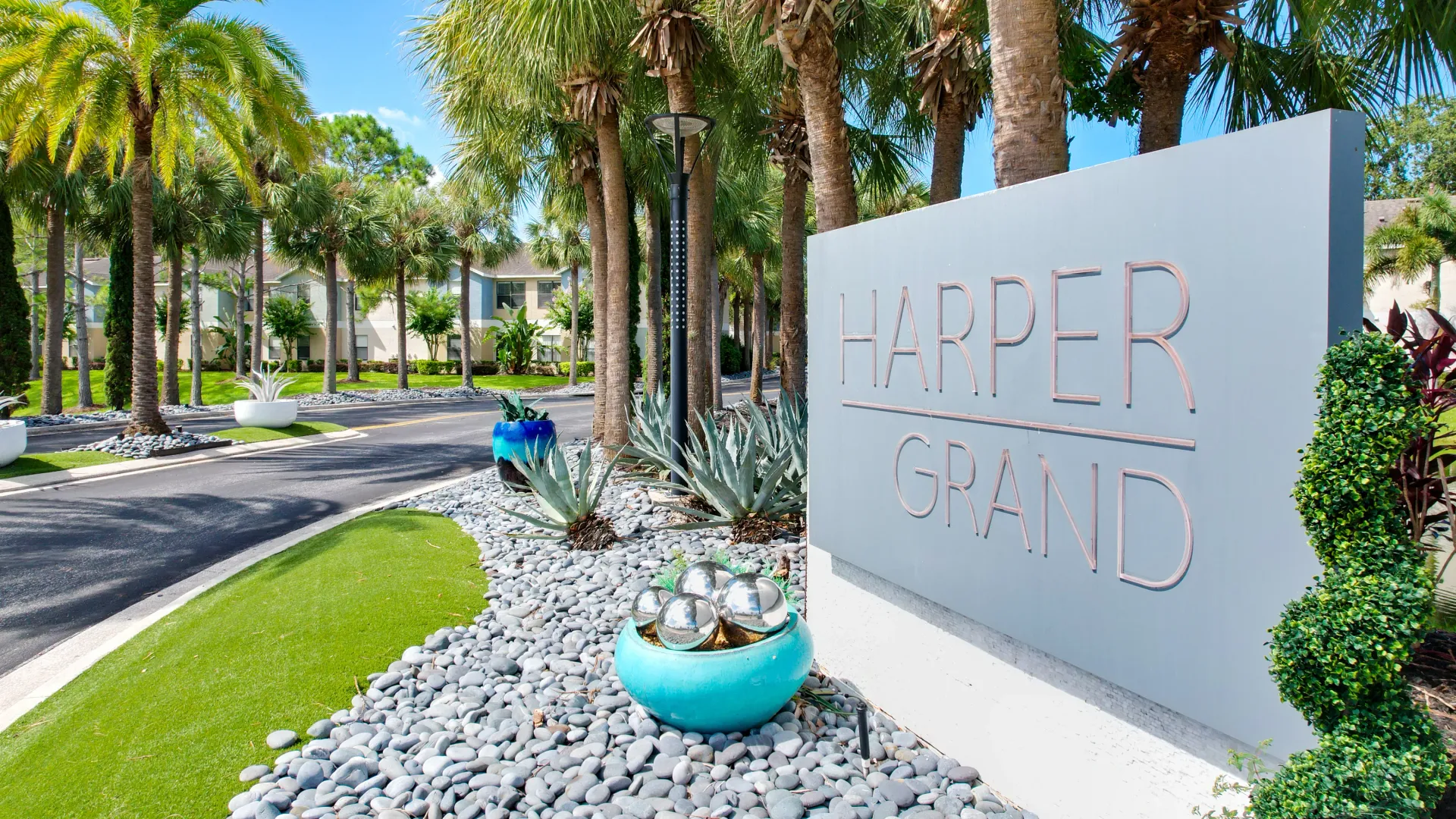 Entrance sign of Harper Grand Apartments with lush landscaping and palm trees.