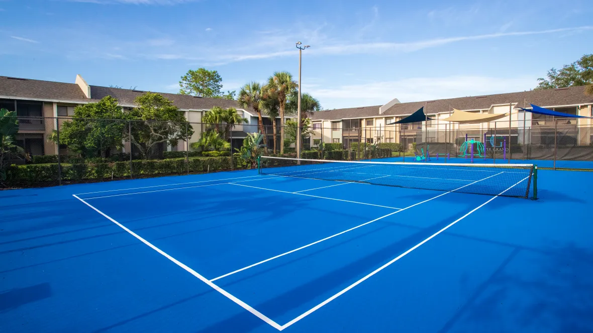 A vibrant blue tennis court nestled between apartment buildings for convenient access to spirited fitness on the court.