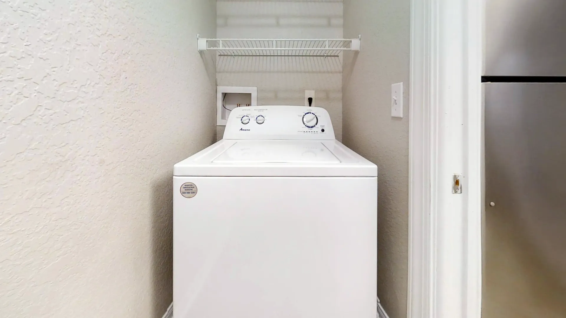 Laundry nook with white top-loading washer and overhead shelf in The Chateau floor plan.