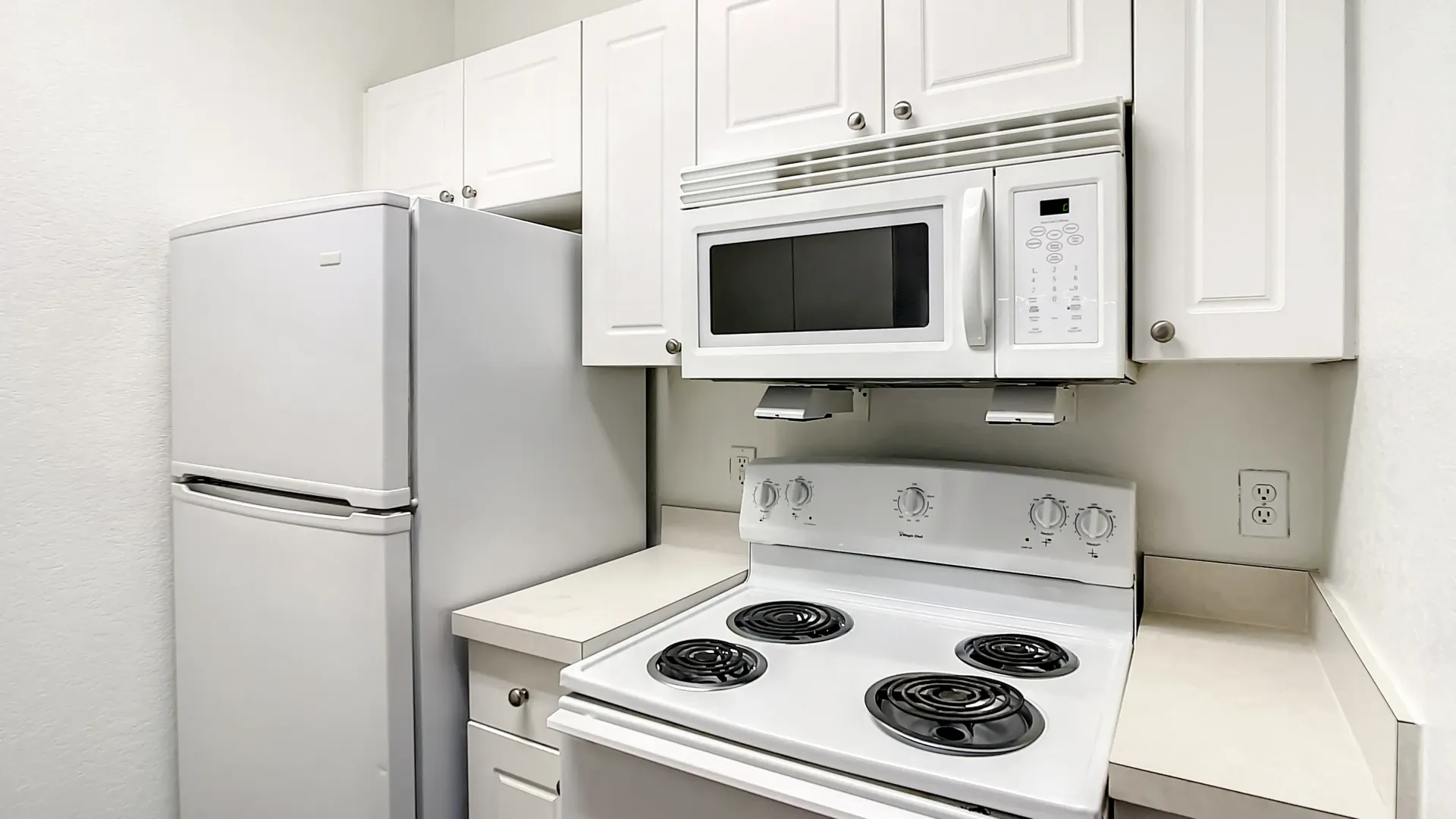 Charleston Cay apartment kitchen with white cabinetry, white appliances, and neutral countertops.