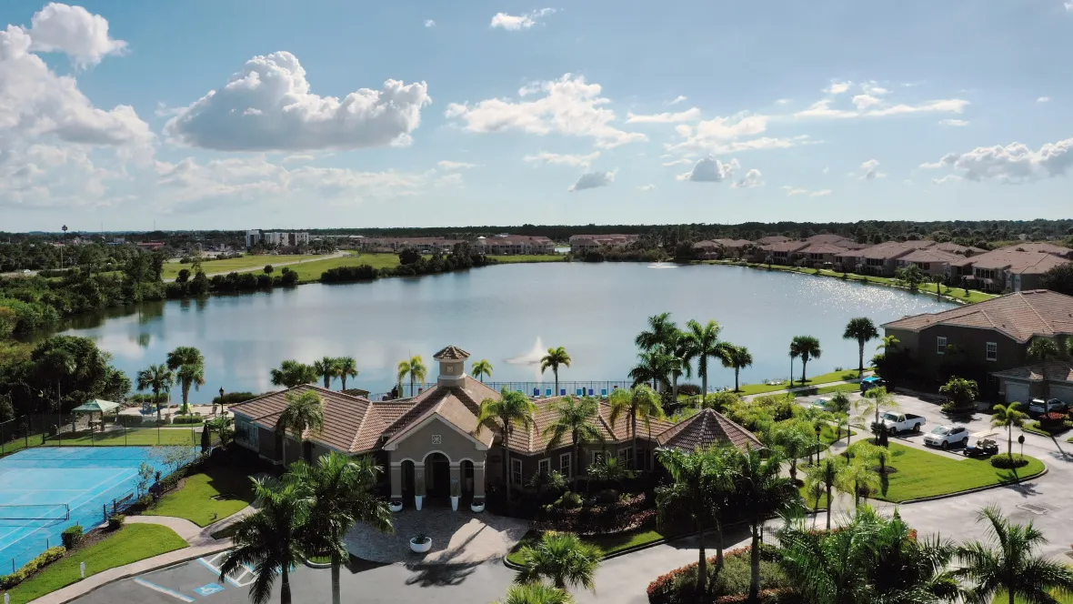 An aerial view capturing the pristine lake, Clubhouse, apartment buildings, and tennis court – a vibrant community that embraces connectedness.
