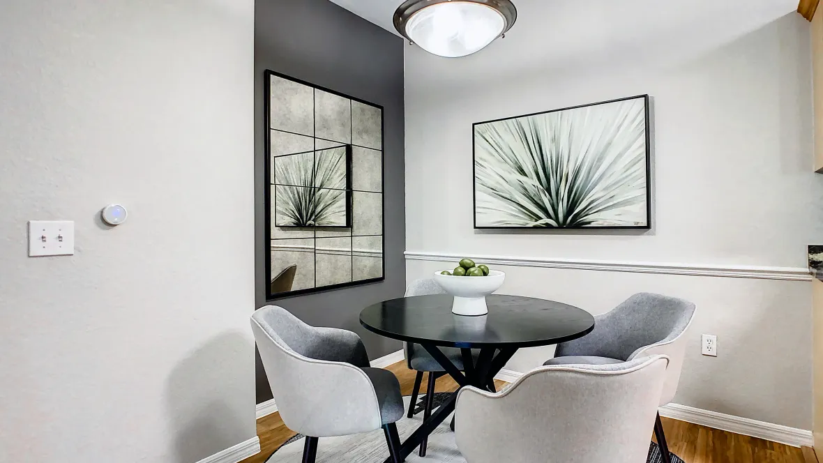 A refined dining area with a large table, seamlessly connecting to the kitchen through a breakfast bar cut-out and a luminous overhead light fixture.