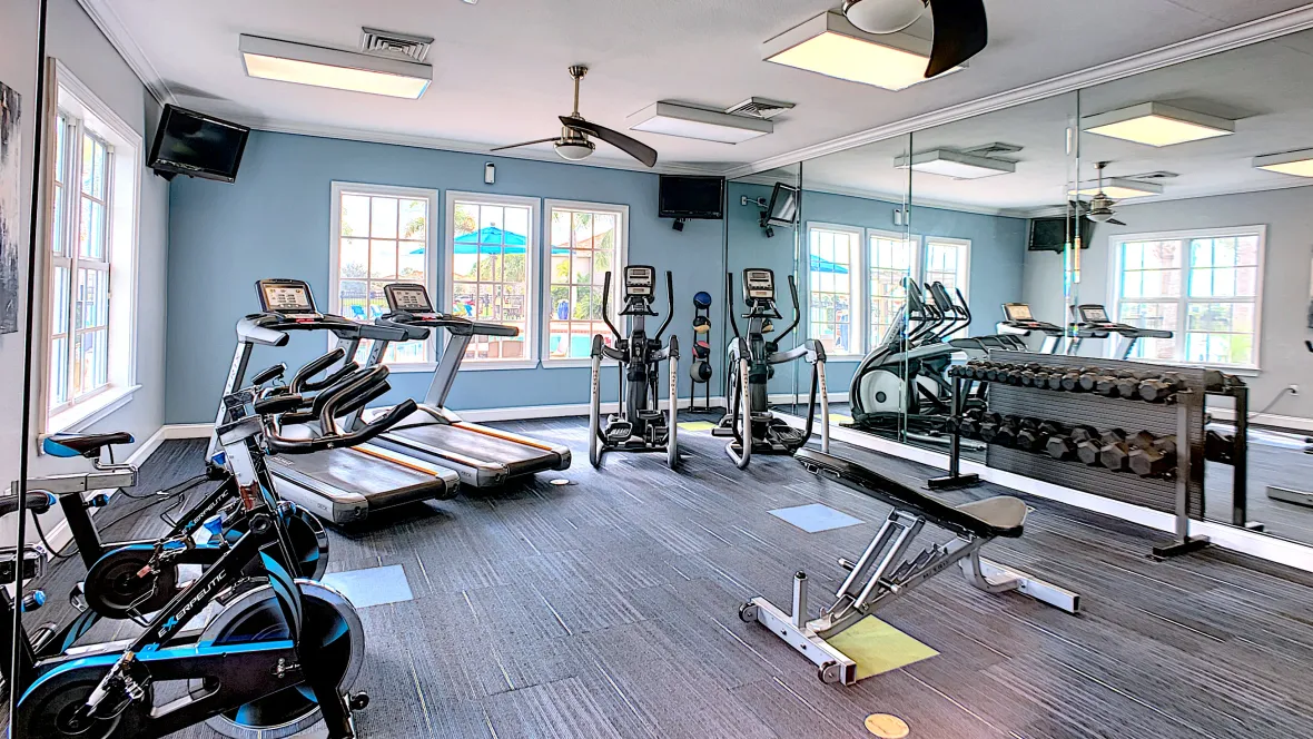 A contemporary resident gym featuring treadmills, spinning bikes, and weight training gear offering abundant overhead lighting and a wall-to-wall fitness mirror.