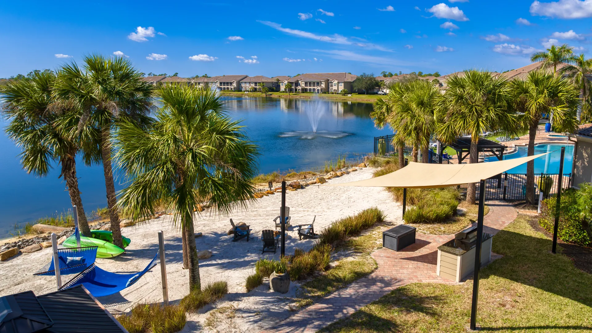 Aerial view of a lakeside beach area with hammocks, a fire pit, and a shaded grilling station.