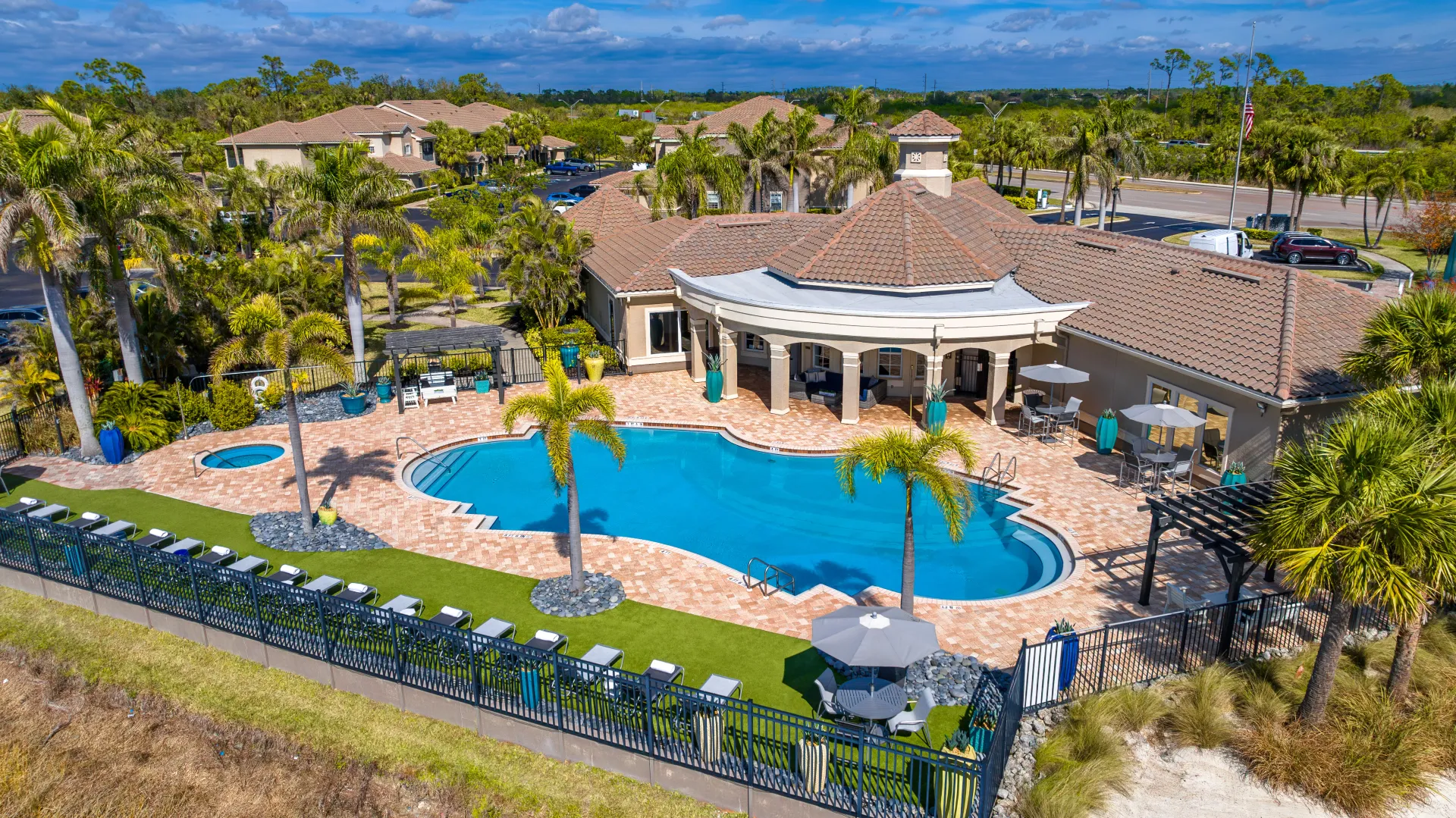 Aerial view of Lakes of Tuscana's resort-style pool with lounge chairs, palm trees, and shaded seating areas.