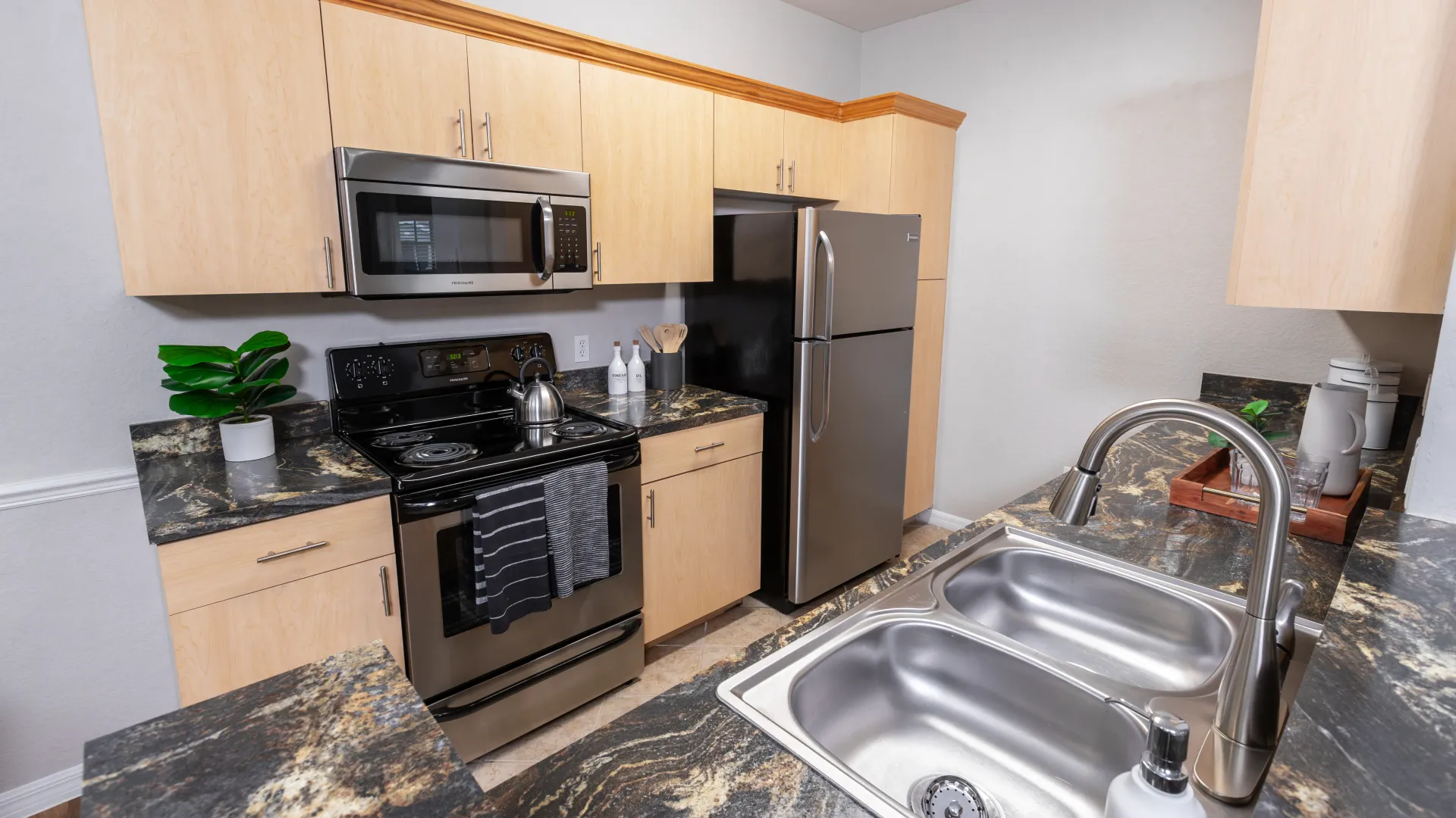 A modern kitchen at Lakes of Tuscana with stainless steel appliances, black granite countertops, and wood cabinetry.