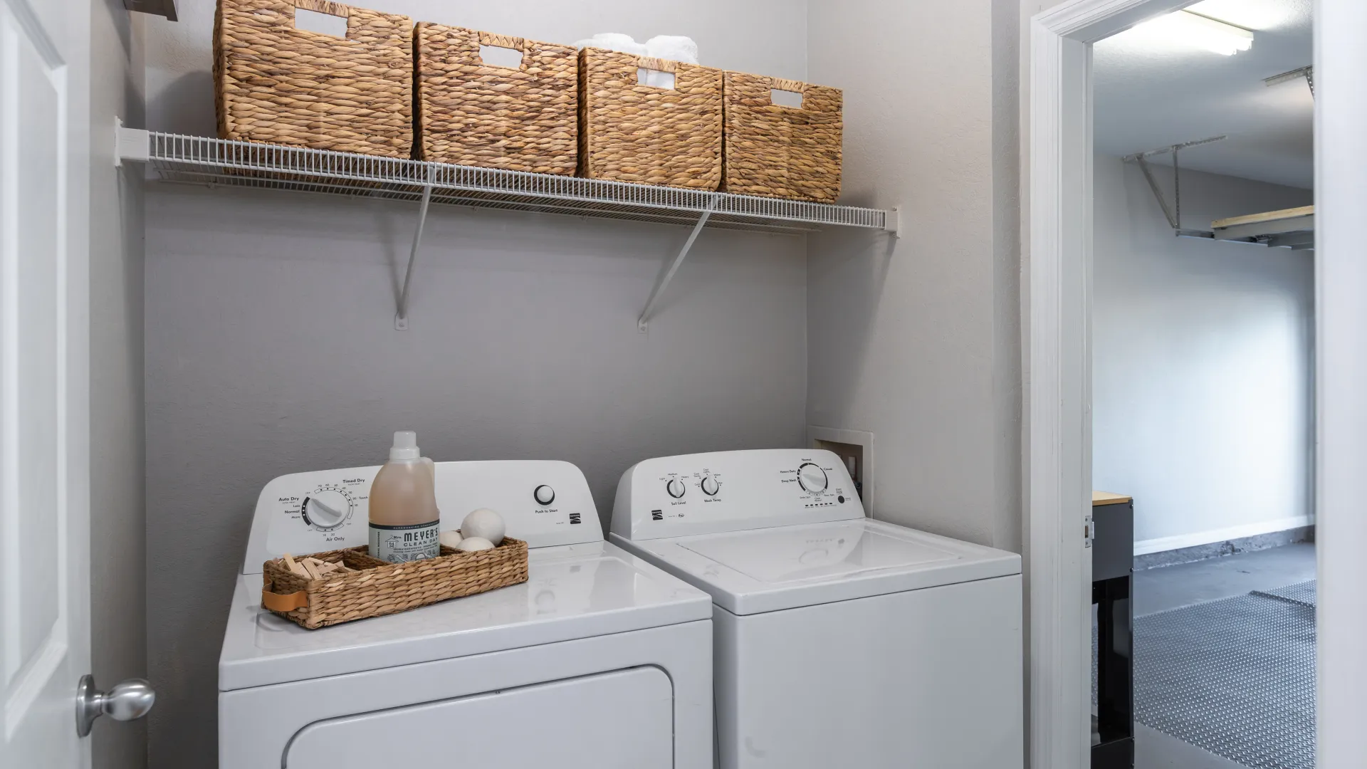 Laundry room with a full-sized washer and dryer, overhead shelving, and woven storage baskets at Lakes of Tuscana.