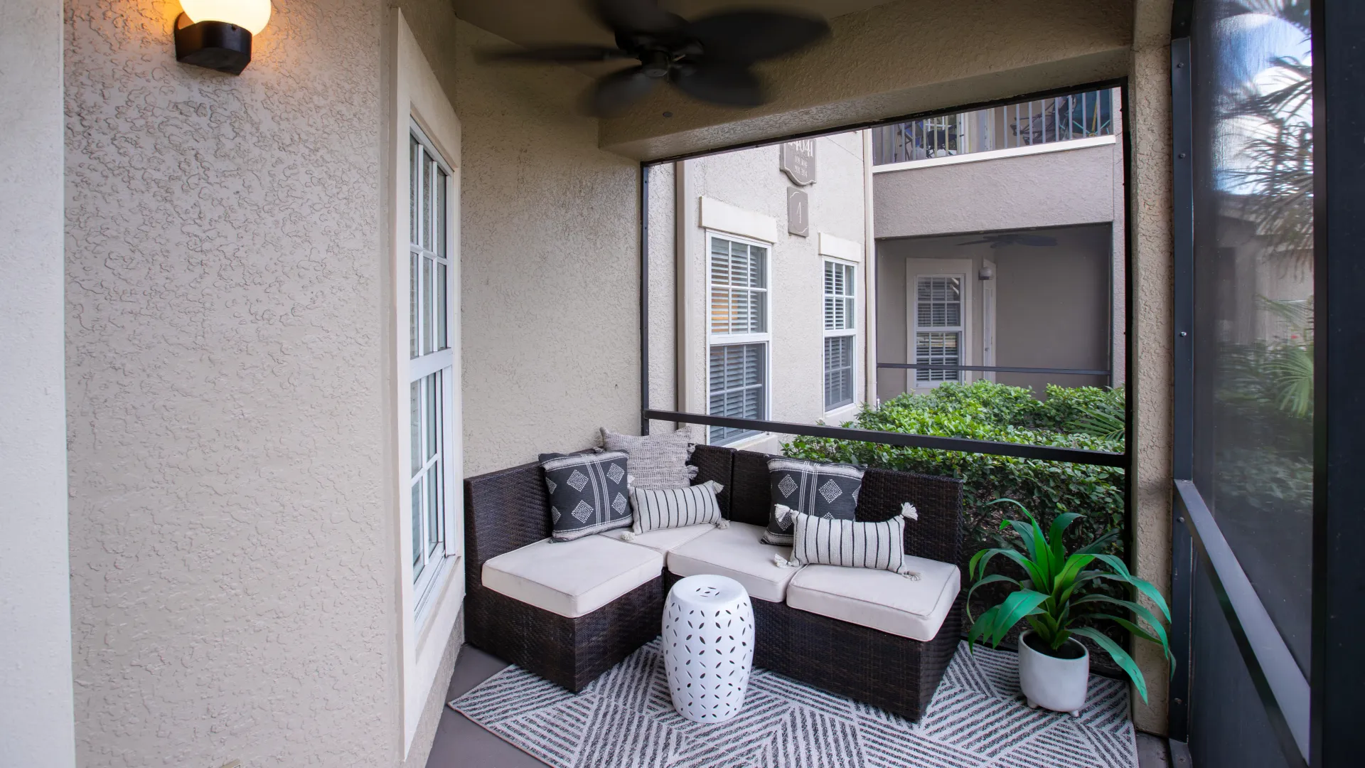 Private screened-in patio with modern outdoor seating, decorative pillows, and lush greenery.