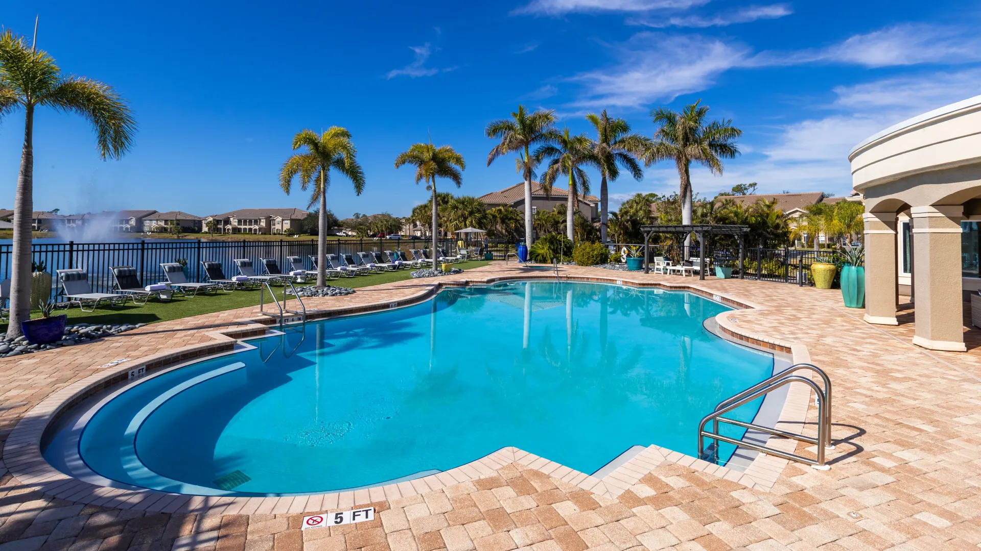 Sparkling pool with tropical landscaping, a pergola seating area, and a peaceful lake setting.