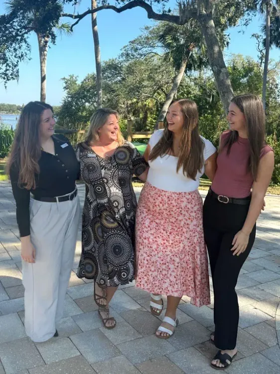Four women from The Preserve at Alafia team laughing and smiling outdoors on a sunny day with trees in the background.