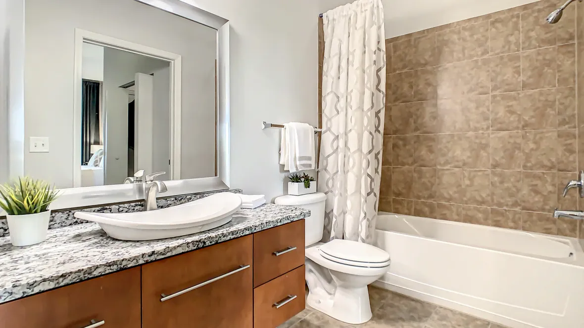 A superiorly spacious bathroom displaying a shower/tub combo, abundant storage, a large mirror, and granite countertops featuring cabinets and drawers below the contemporary bowl sink.