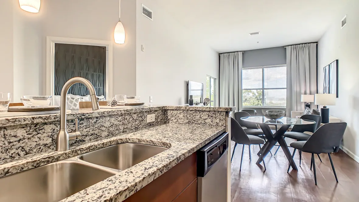 A gourmet kitchen showcasing the sophisticated granite countertops, elegant drop lights hang over the bar-height island, and stainless-steel appliances including a coveted dishwasher next to the deep double sink. 
