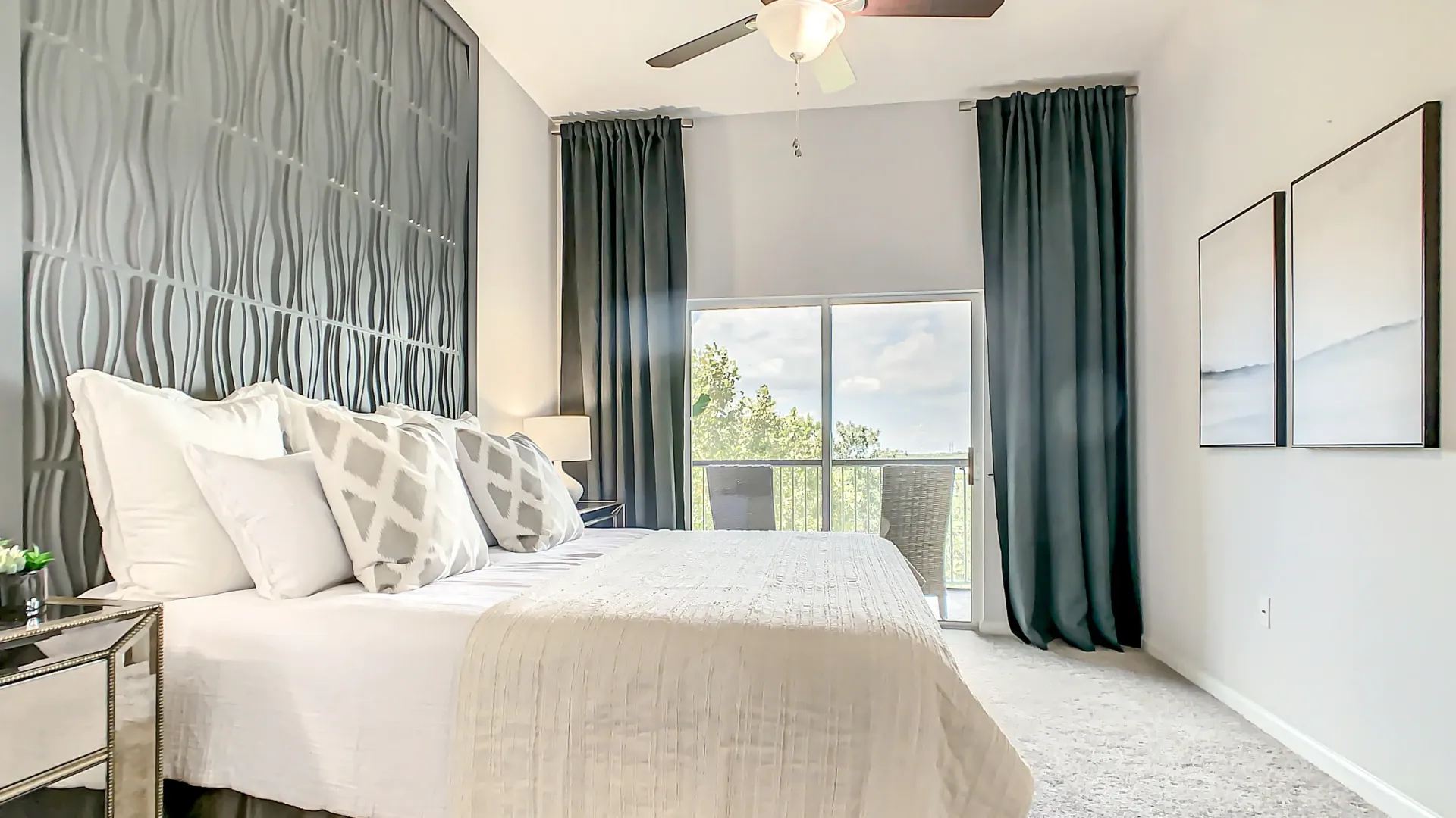 An elegantly appointed master bedroom, outfitted with a king-sized bed, with direct balcony access, flooding the bedroom with natural light, and featuring an overhead lighting ceiling fan.