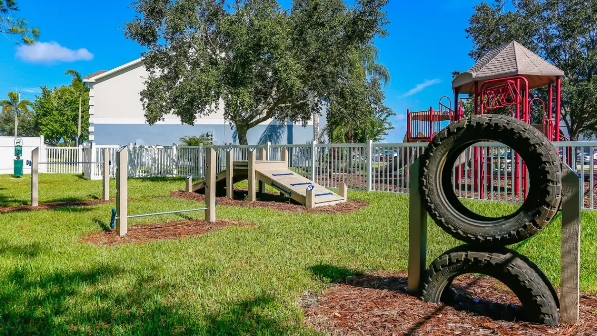 Next to the children’s playground sits a vibrant grassy dog park adorned with an array of agility obstacles including tires for jumps, bars for weaving, and ramps for climbing, offering a fun playground for your furry pal's exercise and enjoyment.