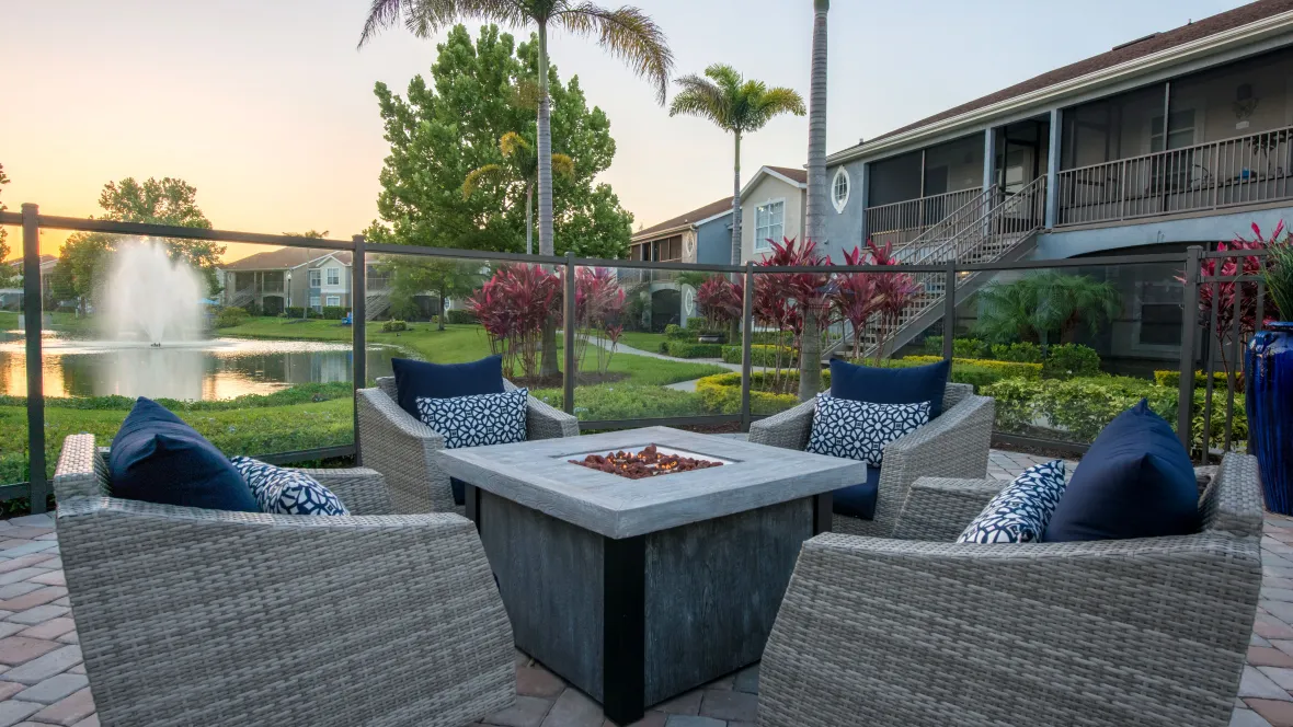 The fire pit aglow with warm light as the sun sets over the spewing fountain lake with hues of pink and gold, creating a picturesque and tranquil evening scene.