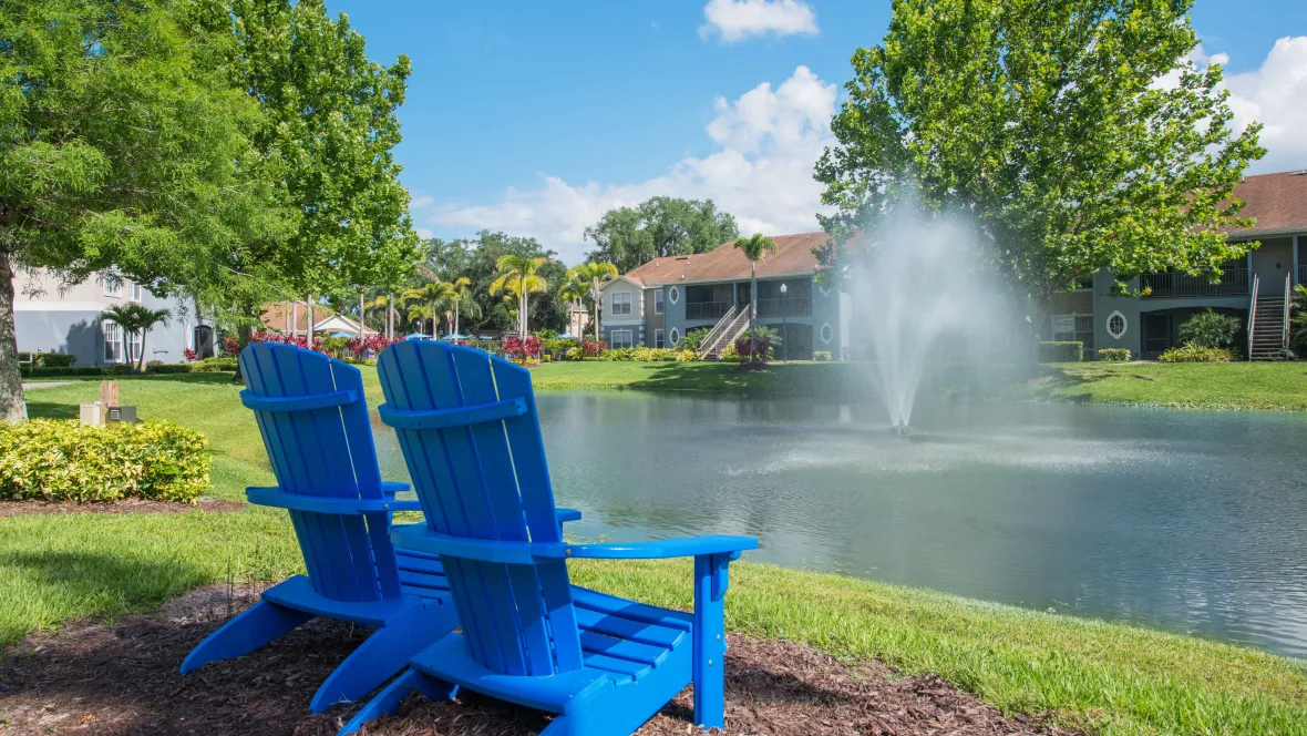  A picturesque view of the lake featuring a bubbling fountain, inviting Adirondack chairs facing the water, and lush greenery surrounding the lake, creating a peaceful ambiance.
