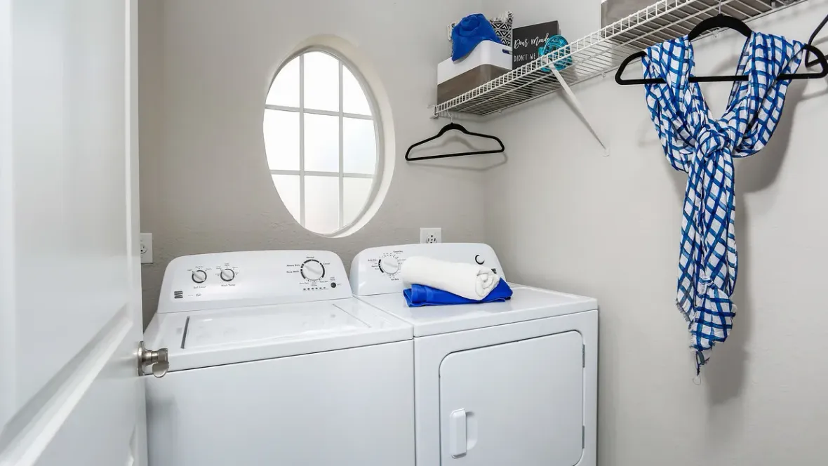 A delightful laundry room nestled off the living room, complete with a full-size washer and dryer set, a charming oval window, and overhead shelving for added storage.