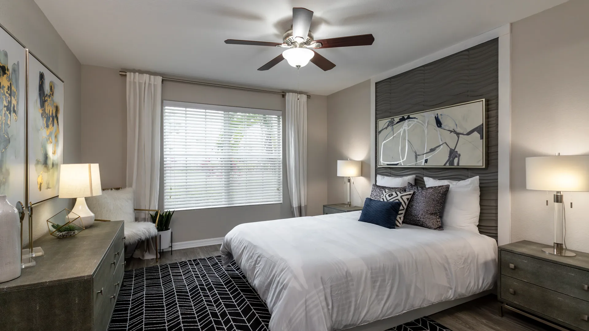 A lavish master bedroom boasting ample square footage with a vast window and generous space for a king-size bed, featuring a breezy ceiling fan.
