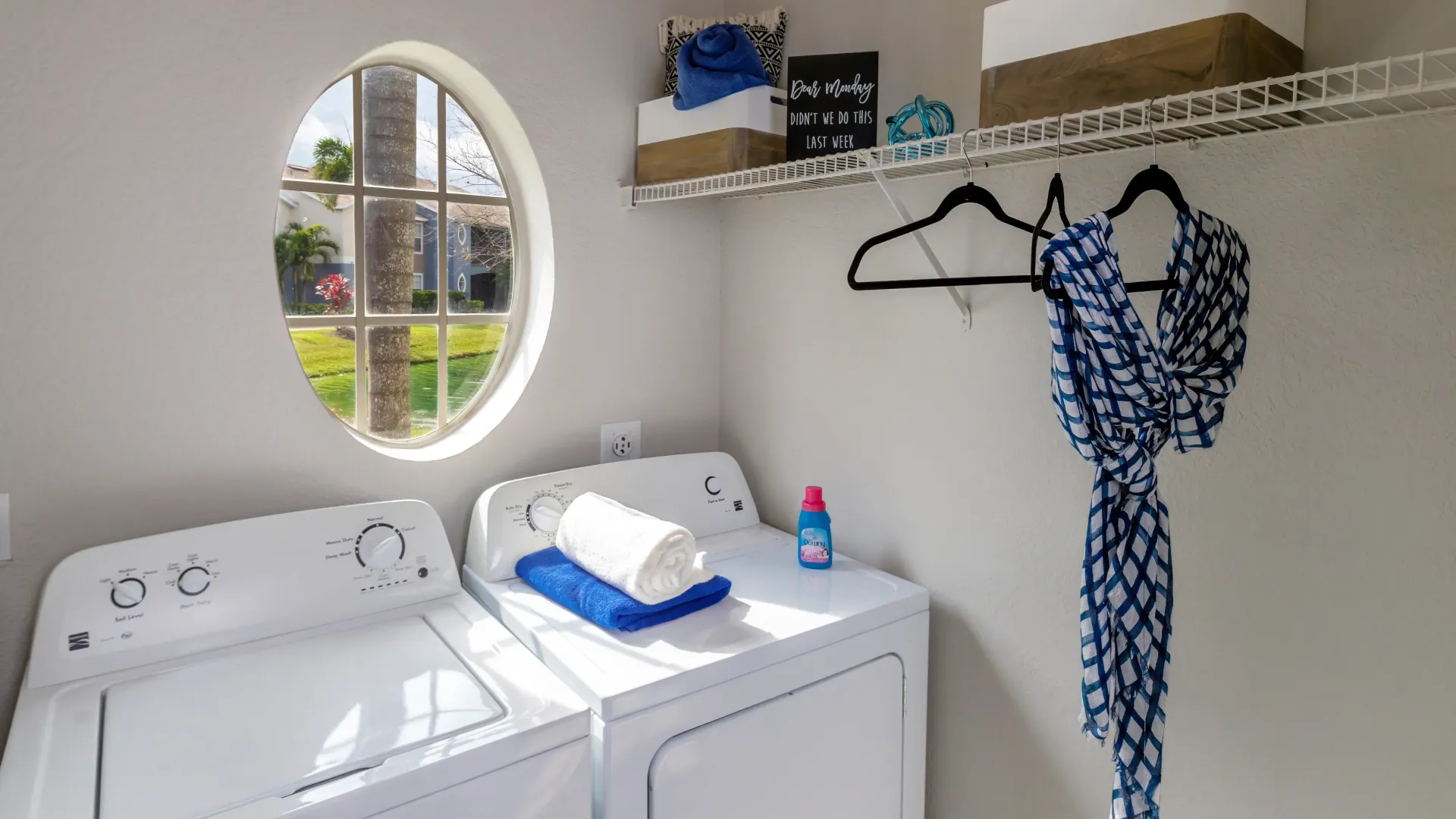 A large, charming oval window lends itself to a brightly lit laundry room equipped with a washer and dryer set with ample storage offered by additional custom shelves. 