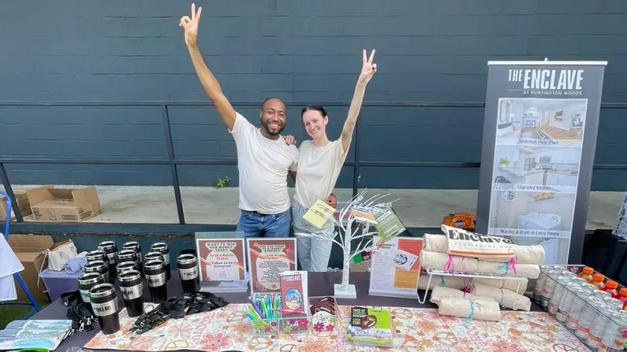 Two members of The Enclave team behind a table set up at a housing fair.