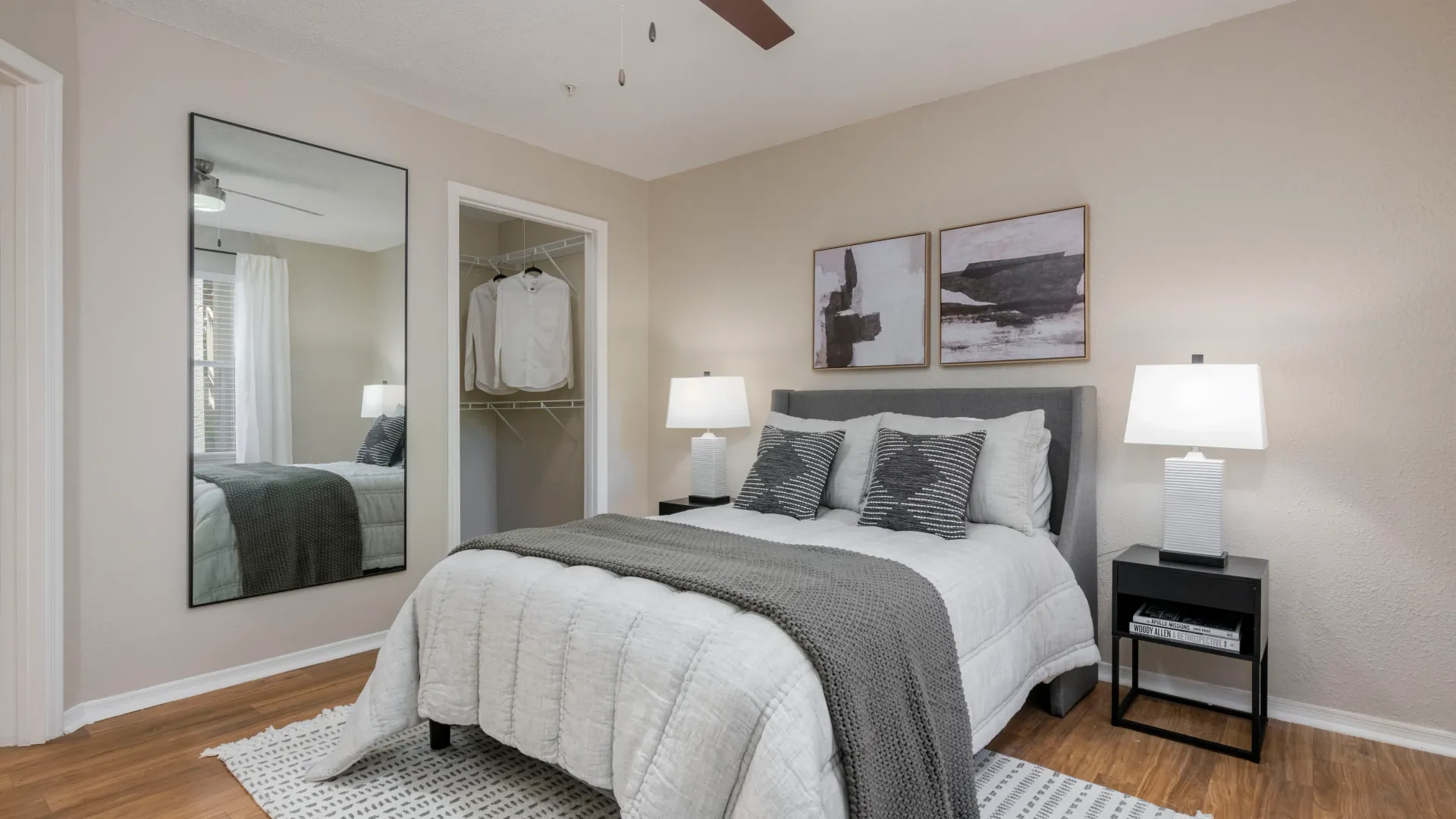 An upgraded bedroom with warm wood-style flooring, a contemporary ceiling fan, and a generously sized closet with built in shelving.