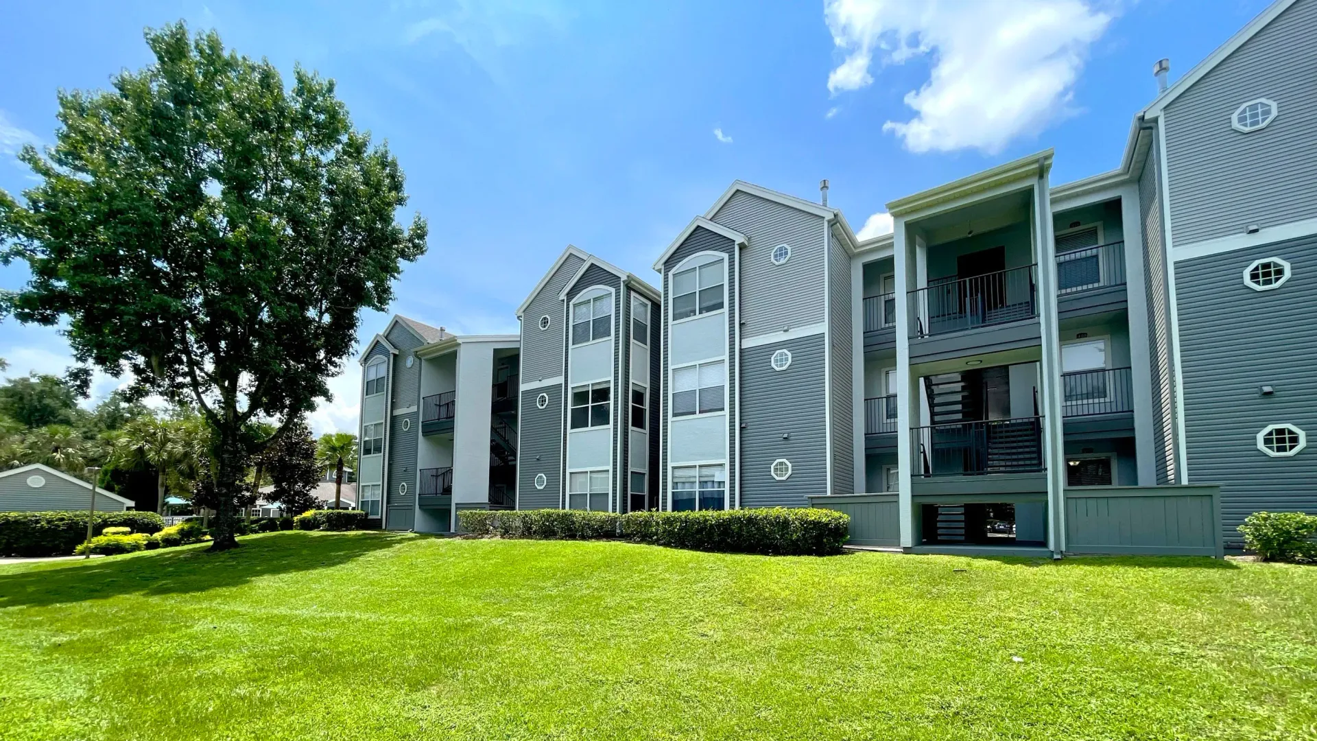 Exterior view of The Enclave at Huntington Woods Apartments, featuring well-maintained buildings with spacious balconies, surrounded by a lush green lawn and trees.