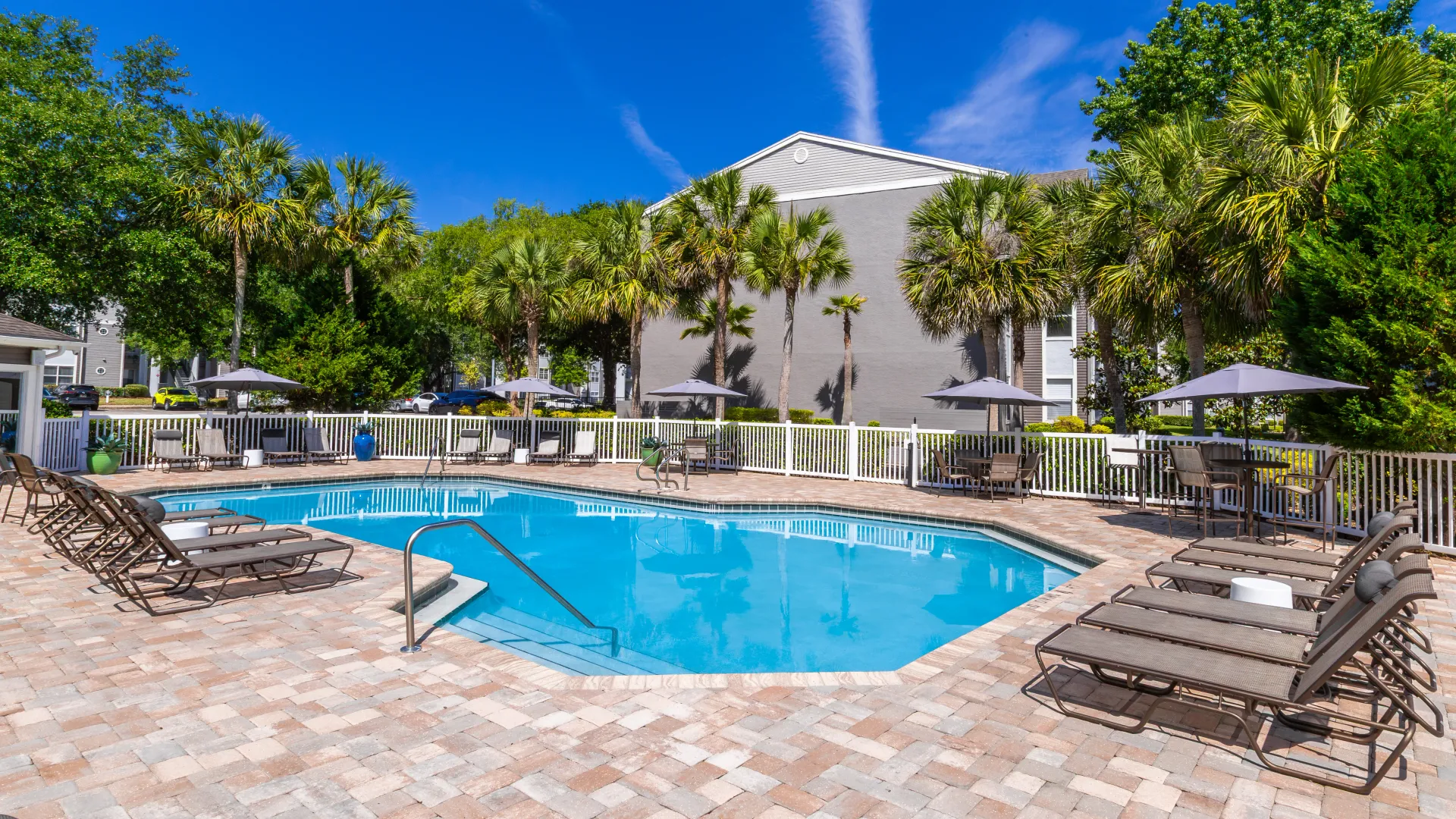 Aerial view of the pool area at The Enclave at Huntington Woods with lounge chairs, patio tables with umbrellas, and surrounding palm trees.