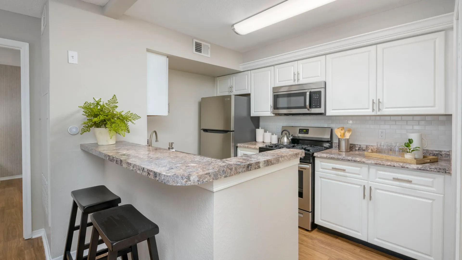 A well-lit kitchen with white cabinetry, gleaming subway tile backsplash, and stylish granite-style countertops.