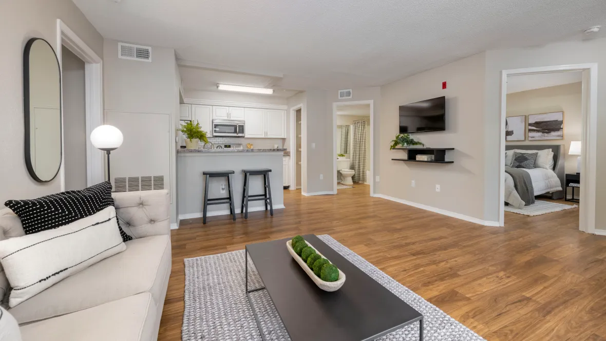 An open living room with wood-style floors, providing a seamless view into the kitchen, guest bedroom and guest bathroom from a single vantage point.