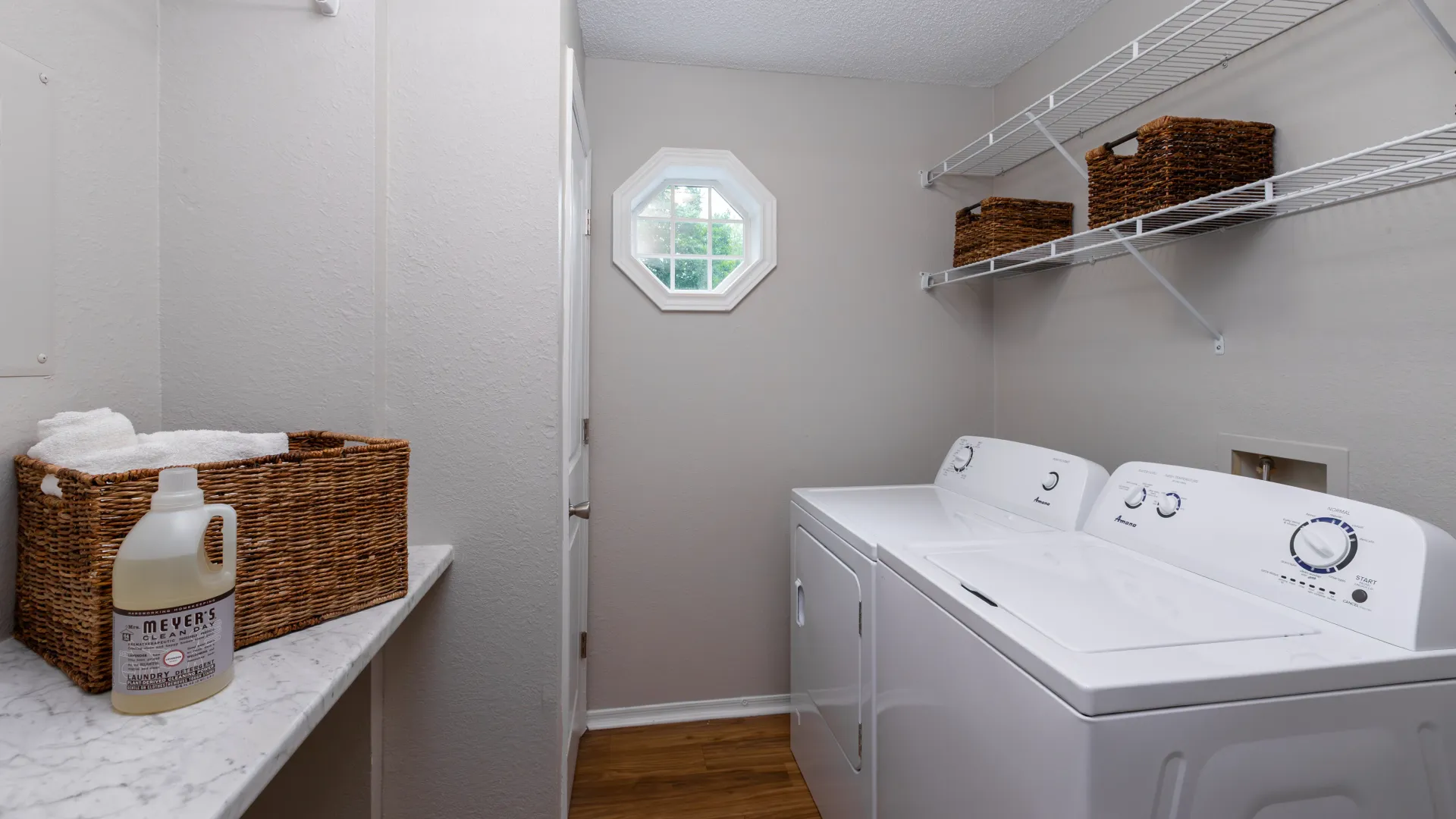 Laundry room with full-size washer and dryer, built-in shelving, and an octagon window letting in natural light.