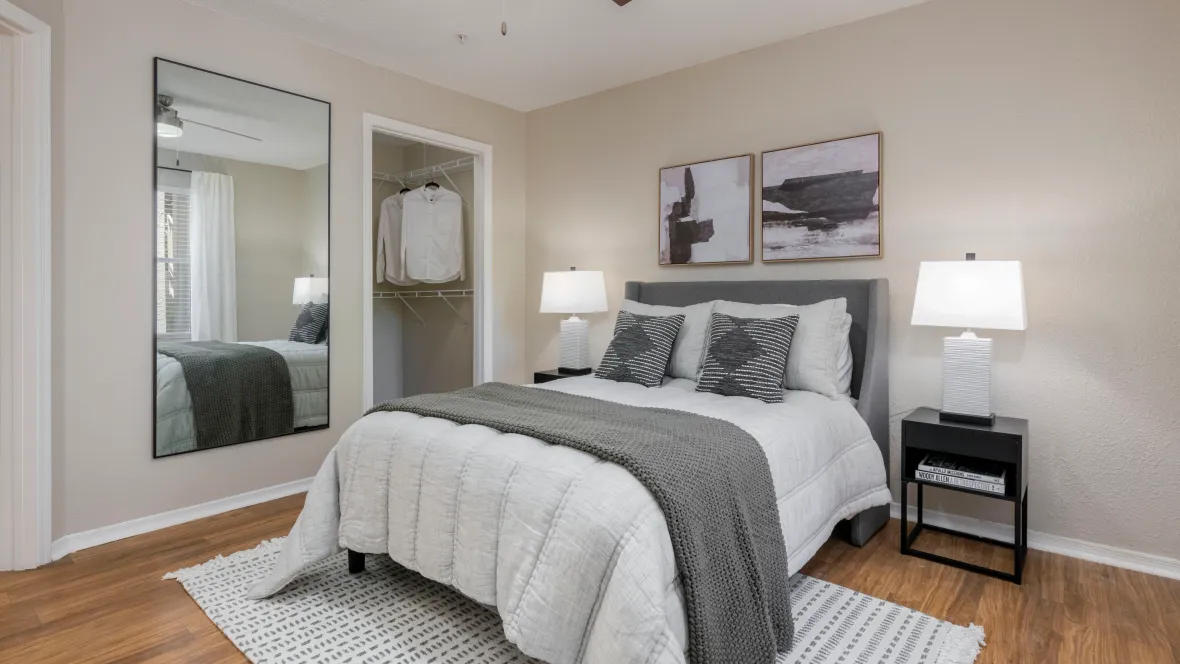 An upgraded bedroom adorned with warm wood-style floors, a modern ceiling fan, and generous closet space with built-in shelving.