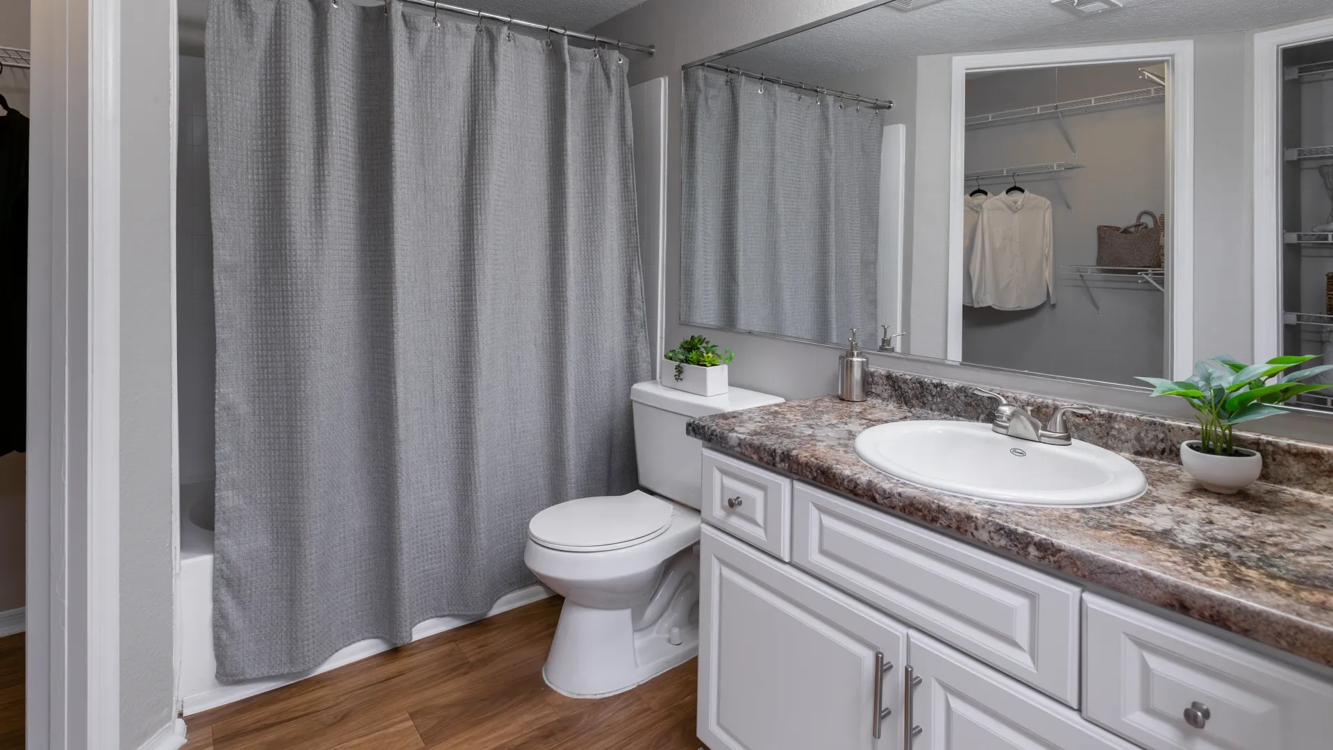 Bathroom at Oasis at 1800 with granite-style countertops, white cabinetry, and gray shower curtain.