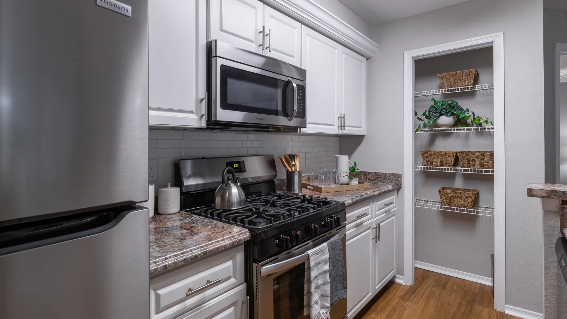 Contemporary kitchen with stainless appliances and open pantry shelves at Oasis at 1800.