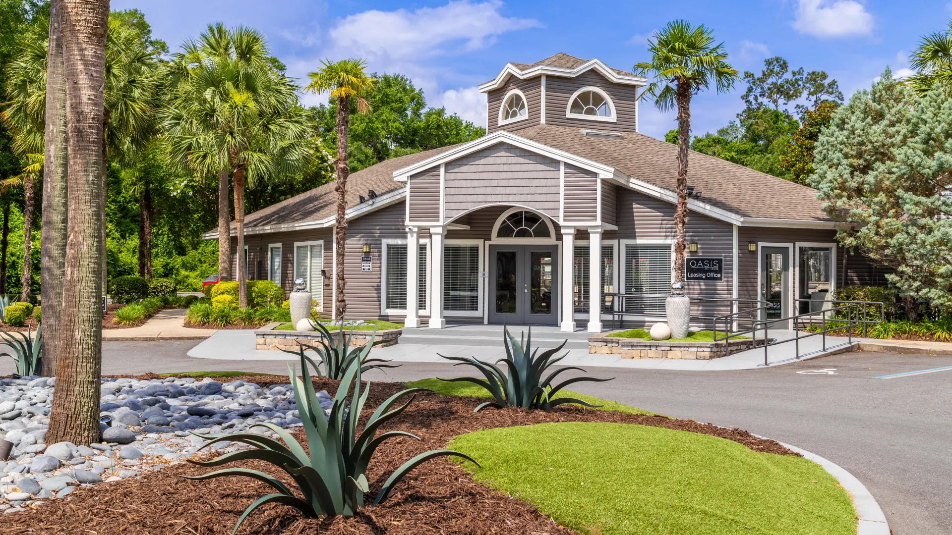 The exterior of the Oasis at 1800 leasing office with palm trees and decorative landscaping.