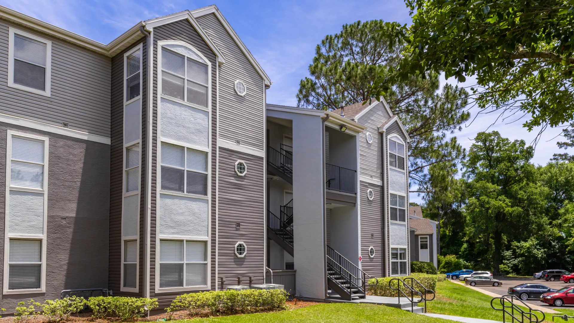 Renovated apartment building at Oasis at 1800 with modern exterior paint and stair access, next to green lawns and trees.