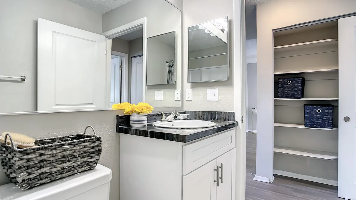A well-lit restroom with a generously sized mirror and an additional mirrored medicine cabinet. Seen across from the open bathroom door, is a convenient linen closet in the hallway for extra storage options.  