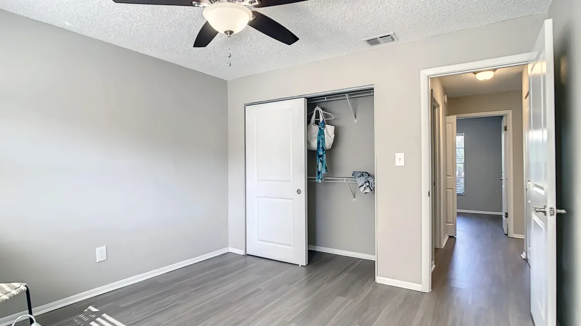 An inviting bedroom with elegant wood-like flooring through extends across the floor plan as well as a generous closet with open wire shelving, and a multi-speed ceiling fan with lights. 