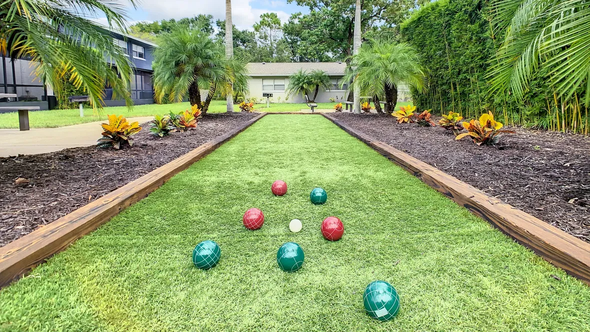 A well-manicured bocce ball court with set up ready for play in a beautiful outdoor setting complete with vibrant palms. 