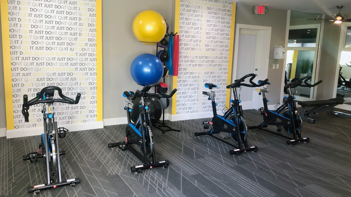 A spinning station with four spin bikes lined up for an exhilarating workout with a motivating message board behind encouraging, “Just Don’t Quit.” 