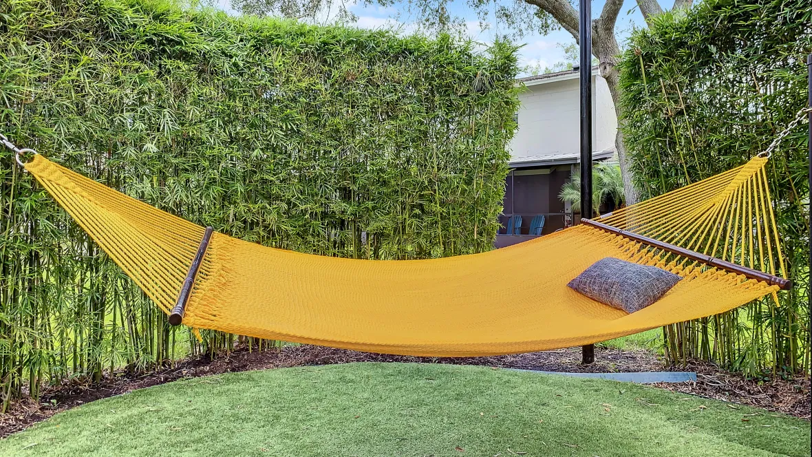 The tranquil hammock garden, a haven for relaxation and sun-soaked naps, with a vibrant mustard-yellow colored, suspended hammock nestled in a cozy bamboo-framed setting. 