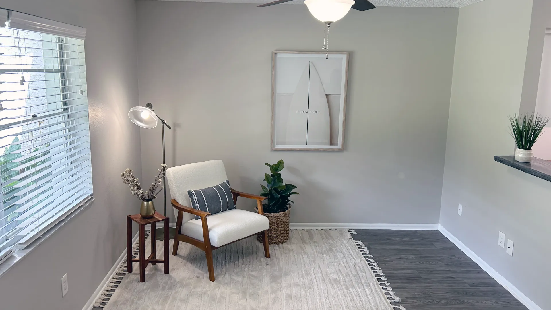 Chic and cozy living space with modern decor, comfortable seating, a large window allowing natural light, and stylish furnishings including a floor lamp, framed artwork, and a potted plant.