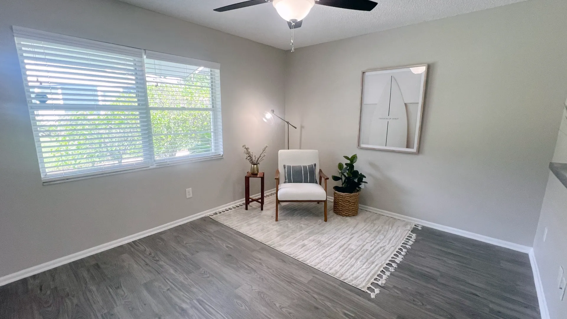 Bright and airy living space with large windows allowing natural light, modern decor, a comfortable chair, a floor lamp, a framed artwork, and a potted plant on a cozy rug.