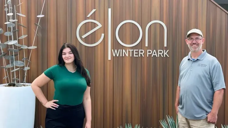 Two team members of Élon Winter Park standing in front of the community sign, representing the friendly and professional staff.