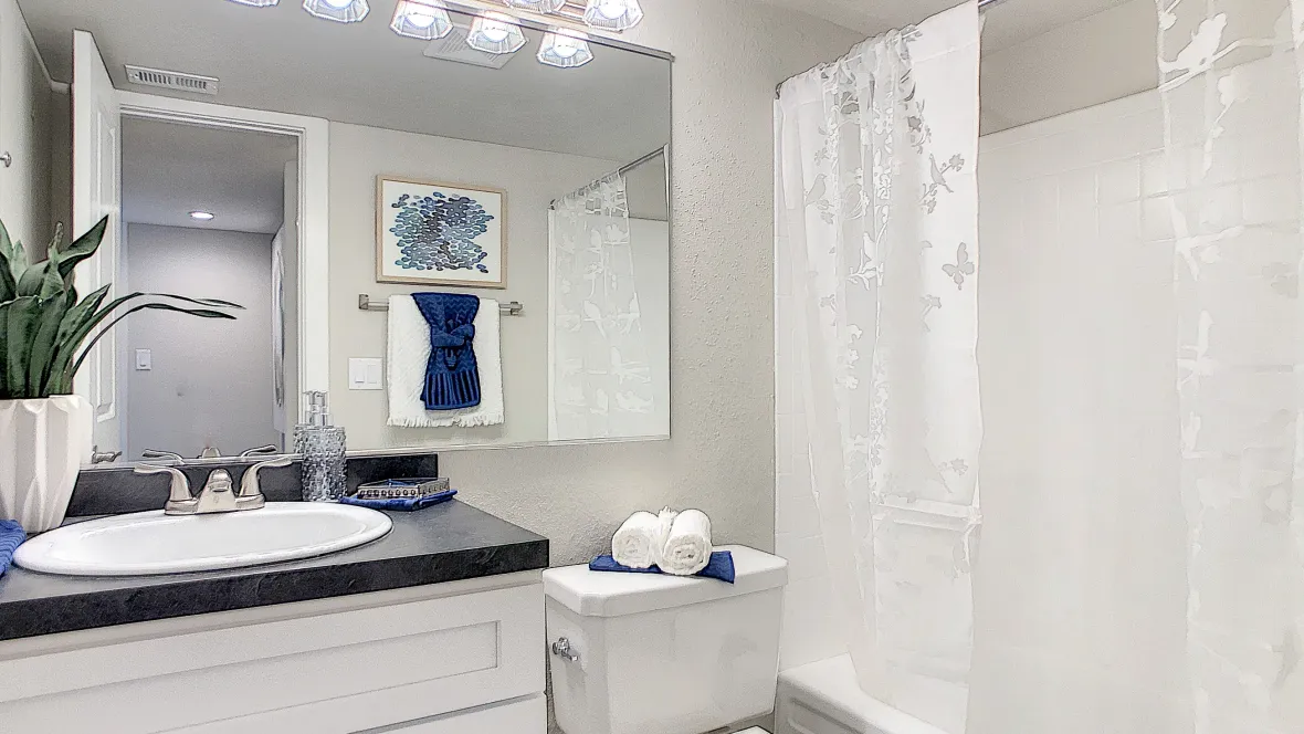 An upgraded bathroom with white cabinetry, black fusion countertops, large mirror, vanity lighting, and garden tub.