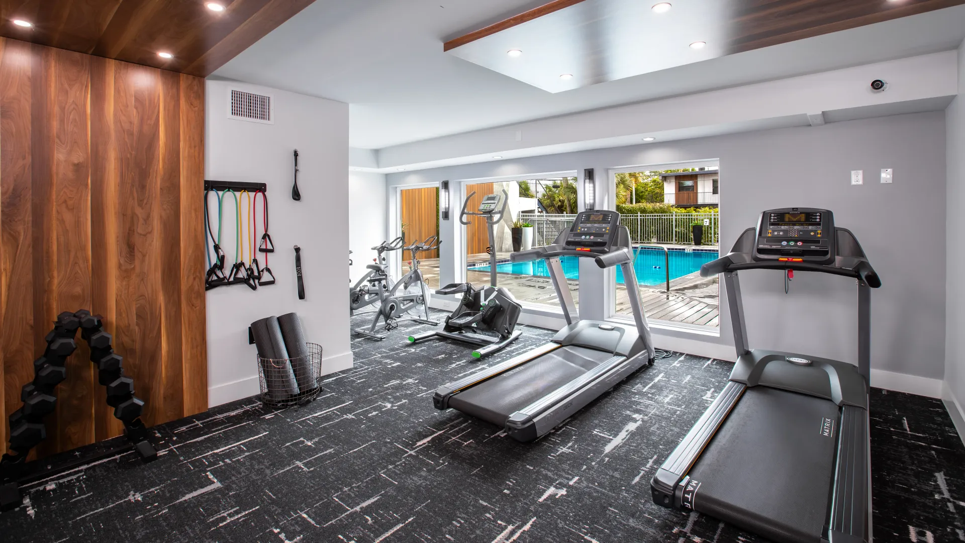 Fitness center at Elon Winter Park Apartments featuring treadmills, exercise bikes, and weight equipment with a view of the pool through large windows.